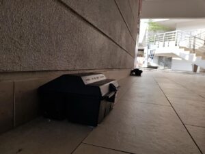 Black rodent bait stations along an exterior building wall on a covered, tiled walkway in Vancouver, BC.